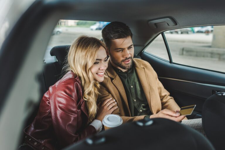 smiling young couple with paper cup and credit card sitting in taxi
